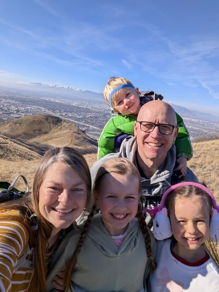 Ben and his family smiling together on a sunny hilltop overlooking a city valley.